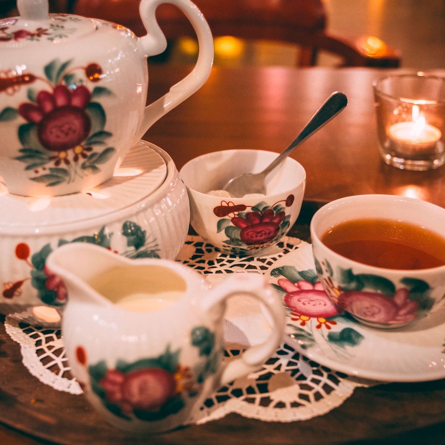 Ein typisch ostfriesisches Teegedeck auf einem Tisch bestehend aus einer Teekanne auf einem Stövchen und einer Schale Kandiszucker, einem Milchkännchen und einer gefüllten Tasse Schwarztee.