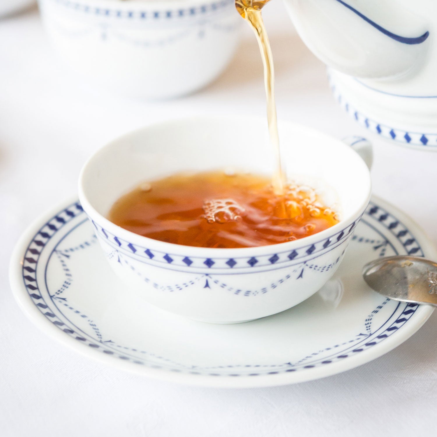 In eine Ostfriesenteetasse wird gerade aus einer Kann Schwarztee gegossen