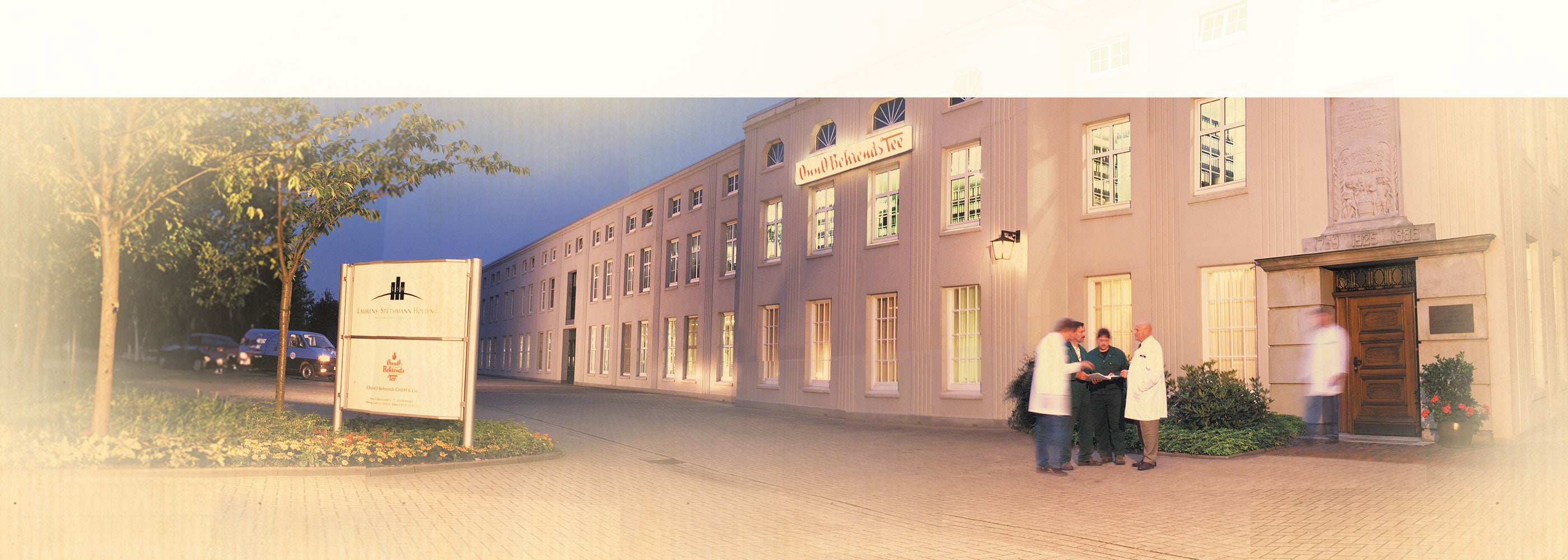 Aktuelle Aufnahme des historischen Gebäudes von Onno Behrends, davor 4 Mitarbeiter in einer Besprechung.