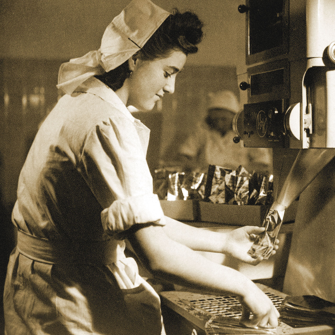 Nostalgisches Foto einer jungen Frau in weißem Kittel und Haarschutz bei der Arbeit an einer alten Tee-Abfüllmaschine