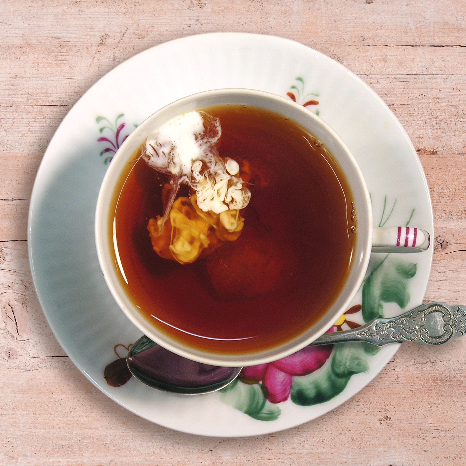 Draufsicht auf eine mit Schwarztee gefüllte Ostfriesenteetasse, in der sich gerade das Milchwölkchen bildet.