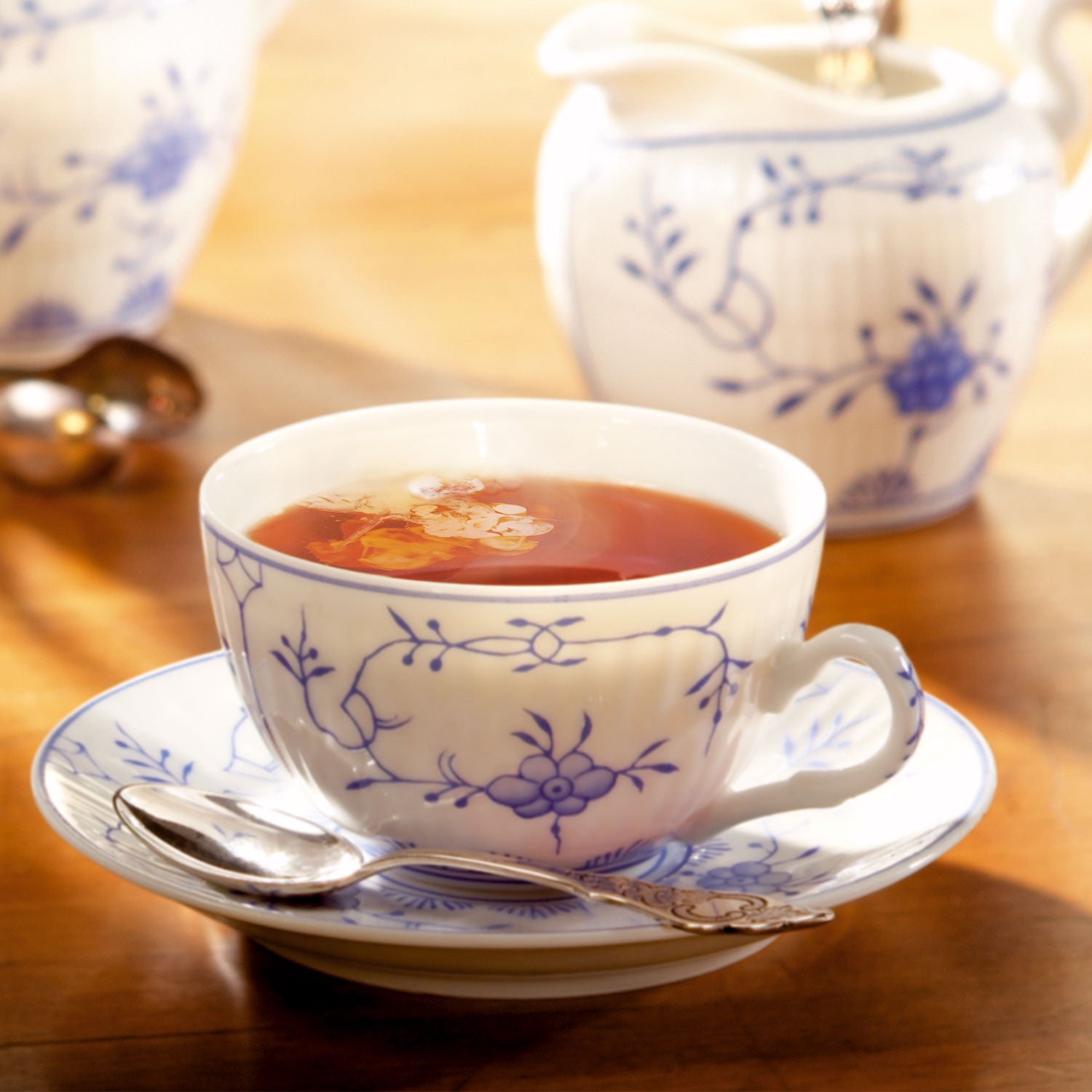 Ostfriesenteetasse gefüllt mit Schwarztee auf einer Untertasse, im Hintergrund ein Milchkännchen.